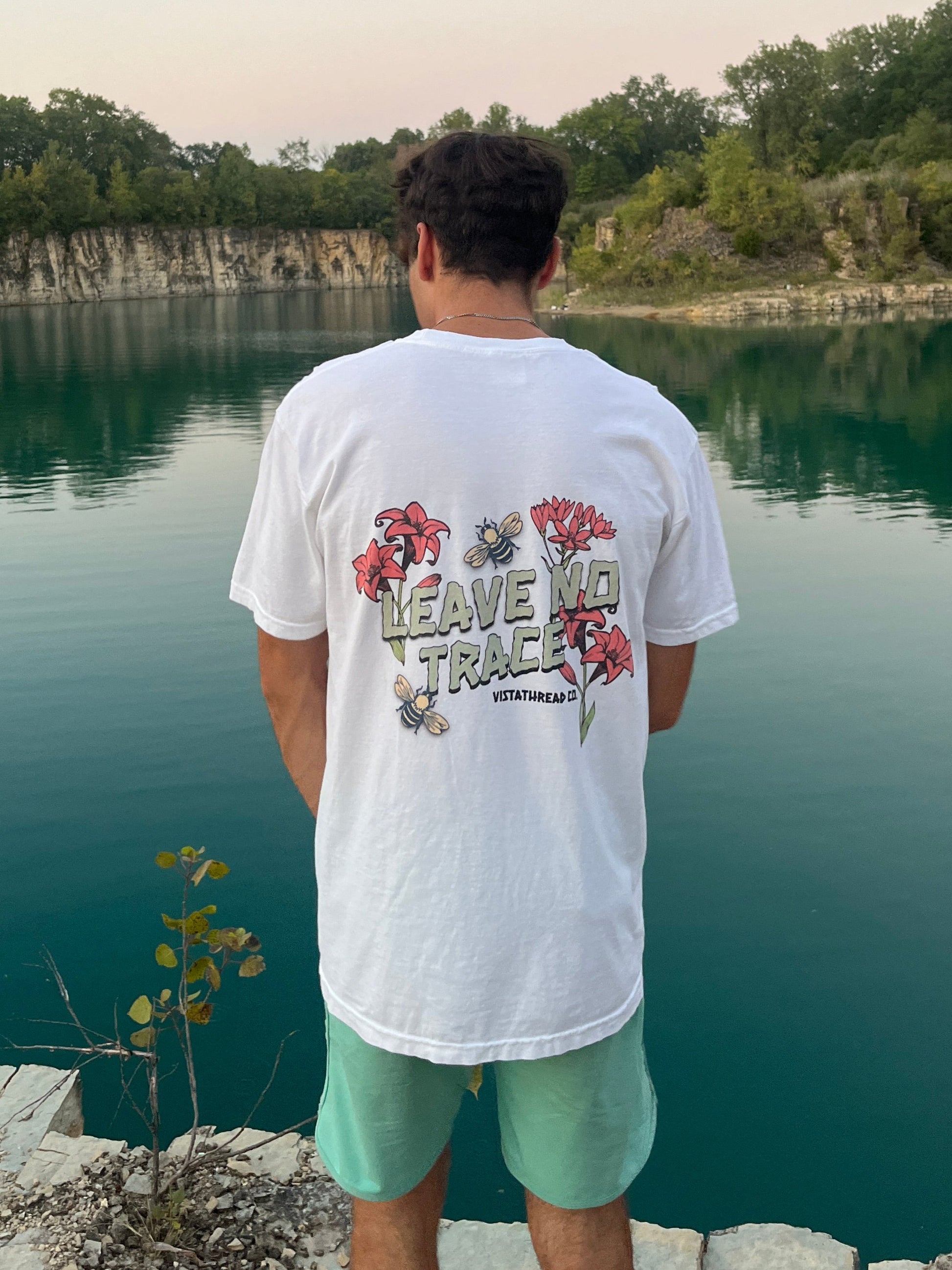 Boy modeling Vistathread Leave No Trace Wildflower t-shirt. Overlooking water on edge of cliff.